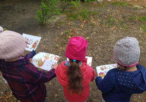 Trzy dziewczynki oglądają wsoje prace plastyczne przedstawiające jesienne liście